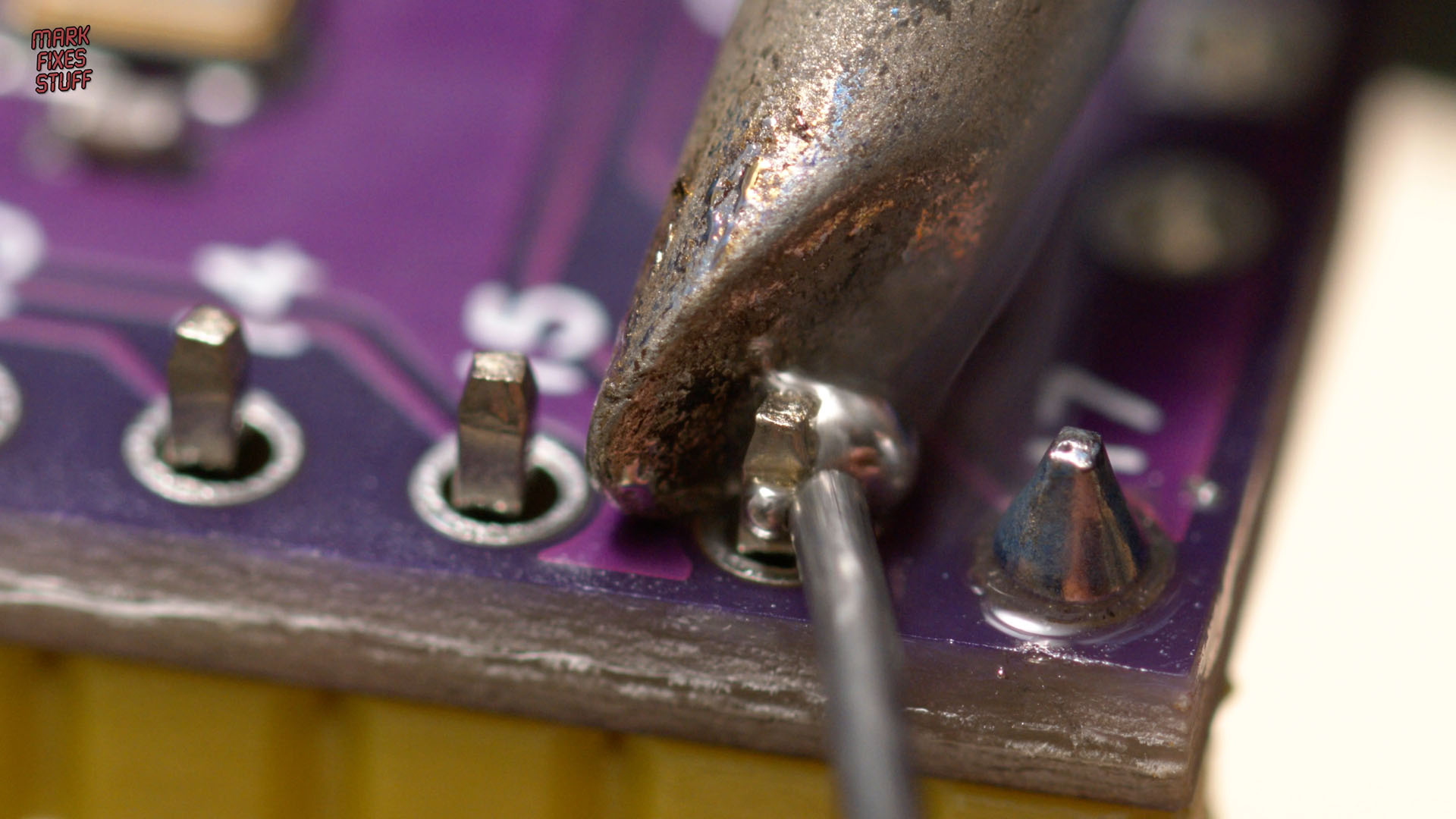 Mark Fixes Stuff soldering a header pin onto a Purple Pico device for an Atari A8PicoCart