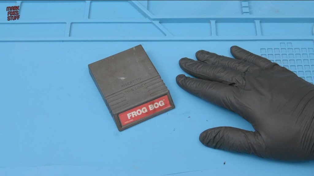 Mattel Intellivision Frog Bog cartridge covered in soot from a house fire, on a blue repair mat